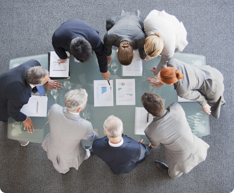 Eine Gruppe von Menschen, die um einen Tisch herum steht und auf Dokumente schaut.